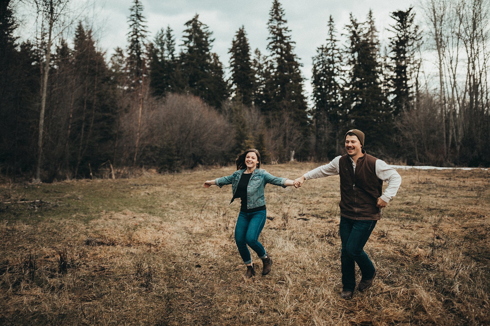 Couple running through field holding hands